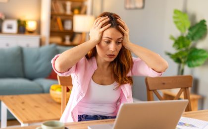 Shocked woman , exhausted from working studying hard. Bored and frustrated looking at laptop. Head resting on hand. Bright space big windows. At home concept. Stress concept.