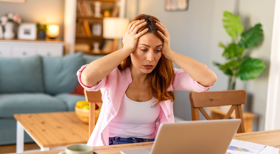 Shocked woman , exhausted from working studying hard. Bored and frustrated looking at laptop. Head resting on hand. Bright space big windows. At home concept. Stress concept.
