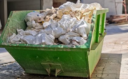 Industrial Dumpster Full of Construction Debris and Rubble on Urban Street. Building Renovation Waste Management and Cleanup Concept